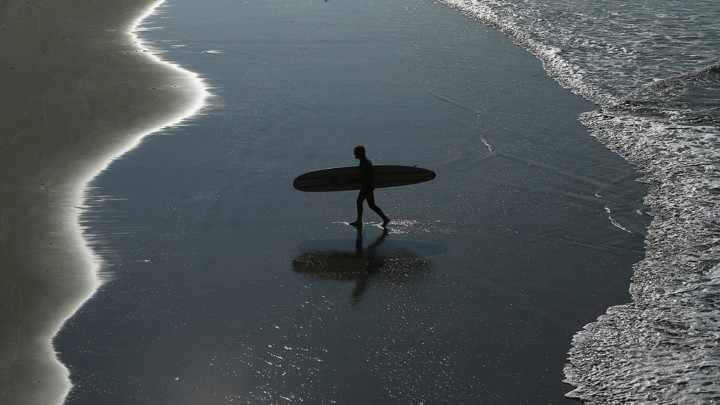 A surfer walks on the beach.