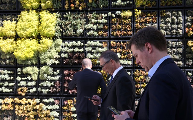 People look at their cell phones in front of a wall garden during the Milken Institute Global Conference in Beverly Hills, California, in May 2017.