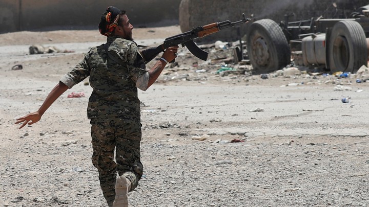 A Kurdish fighter from the People's Protection Units (YPG) fires his rifle at Islamic State militants as he runs across a street in Raqqa, Syria.