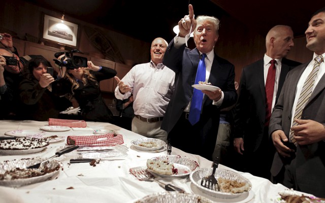 Donald Trump stands eating pie. 