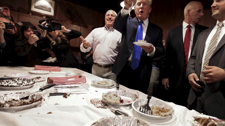 Donald Trump stands eating pie.