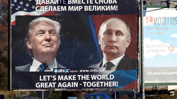 Pedestrians cross the street behind a billboard showing a pictures of President Trump and Russian President Vladimir Putin.