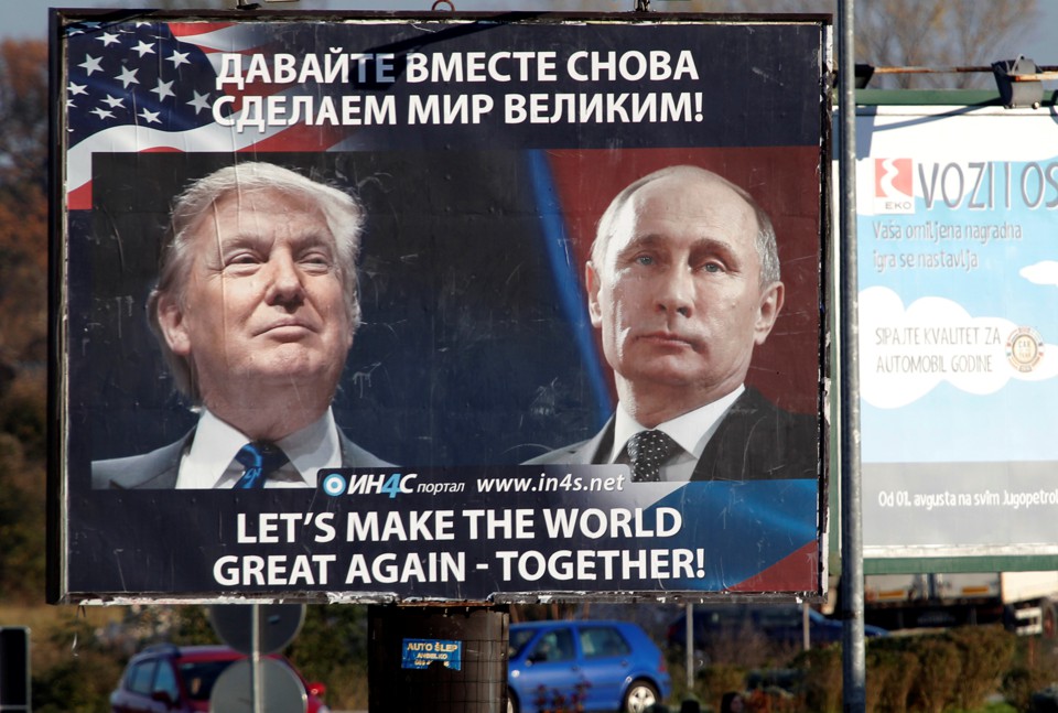 Pedestrians cross the street behind a billboard showing a pictures of President Trump and Russian President Vladimir Putin.