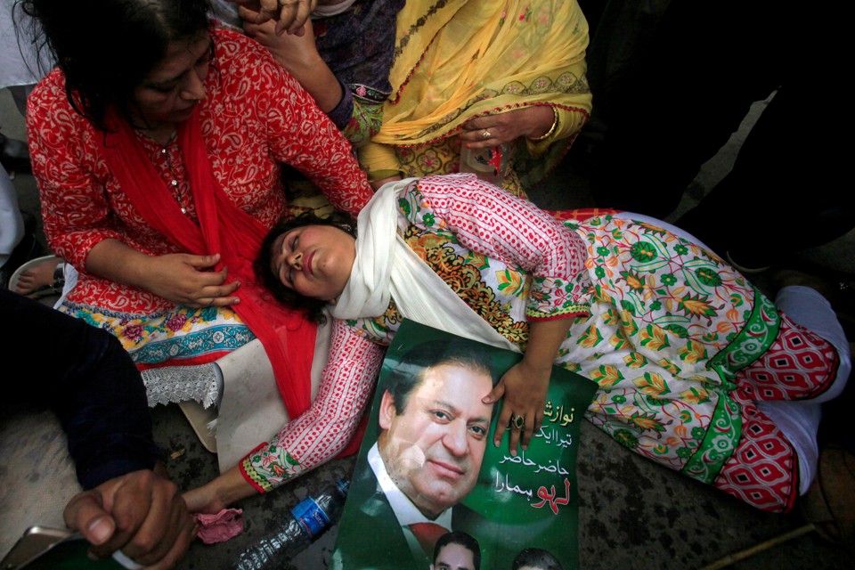 A supporter of Pakistan's Prime Minister Nawaz Sharif passes out on the ground, holding a photo of him.