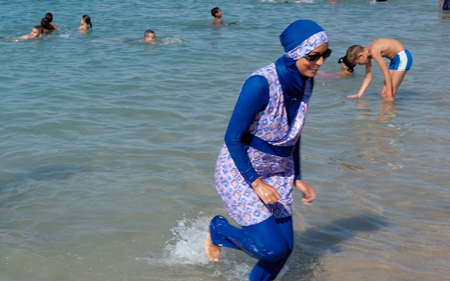 A woman wearing a burqini walks in the water on a beach in France.