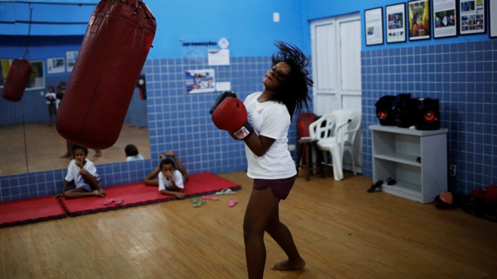 A girl stands next to a punching bag, looking like she is about to punch.