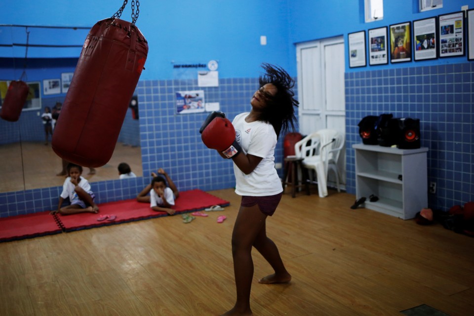 A girl stands next to a punching bag, looking like she is about to punch. 