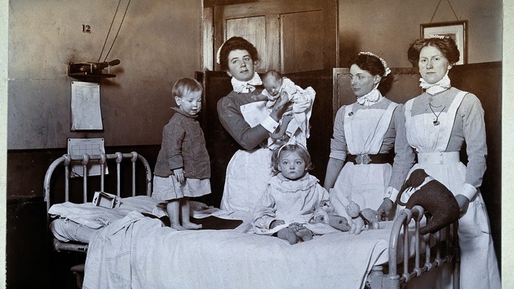 A black-and-white photograph of three women and three young children standing around a bed
