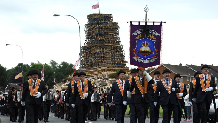 Participants in an Orange Order parade march past a bonfire pyre in Portadown, Northern Ireland.