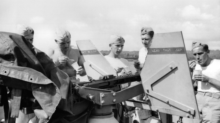 Young American soldiers in the South Pacific stand behind an anti-aircraft gun while eating ice cream, 1943