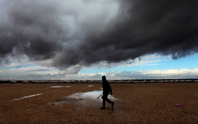 A Syrian refugee walks toward his tent at Zaatari refugee camp through puddles and in front of storm clouds.