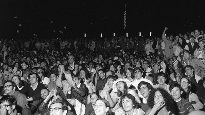 A group of people cheer with an American flag in the background.