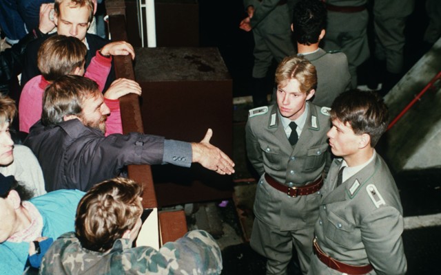 East German border policemen refusing to shake hands with a Berliner over the border fence in November, 1989