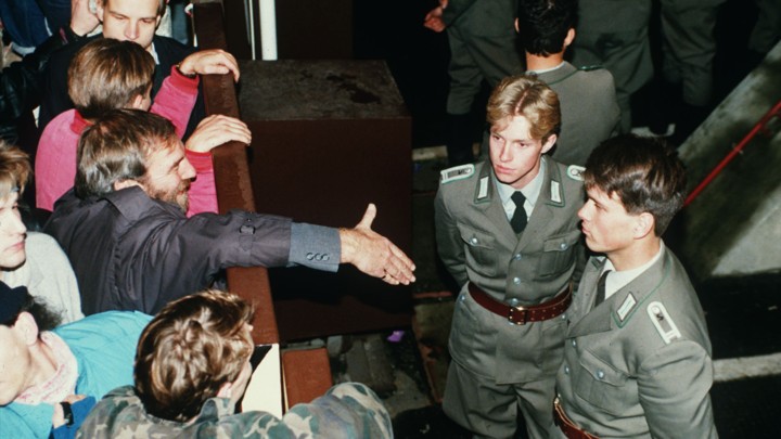 East German border policemen refusing to shake hands with a Berliner over the border fence in November, 1989