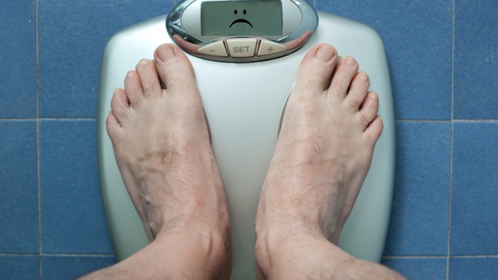 A person stands on a scale displaying a frowning face.