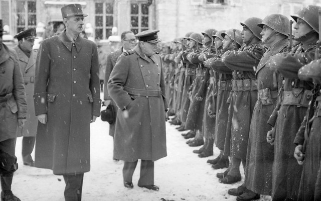 Winston Churchill and General De Gaulle walk past assembled French soldiers under a snowstorm.