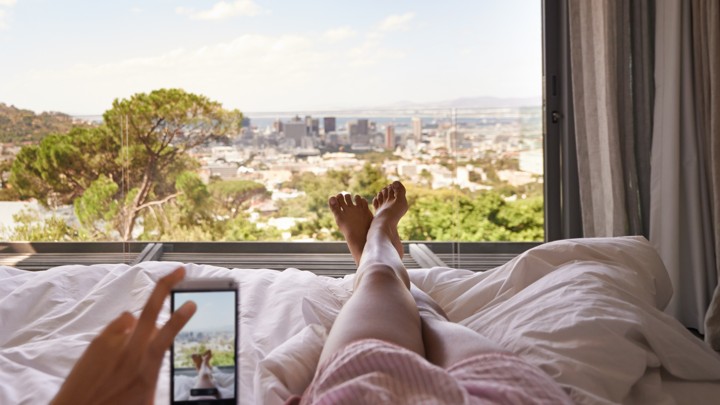 A woman takes a picture of herself lying in bed, overlooking city in the distance