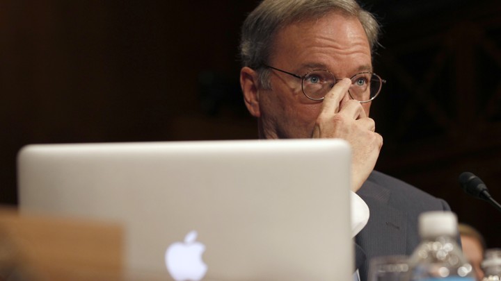 A man sitting behind an Apple laptop covers the lower half of his face with his hand.