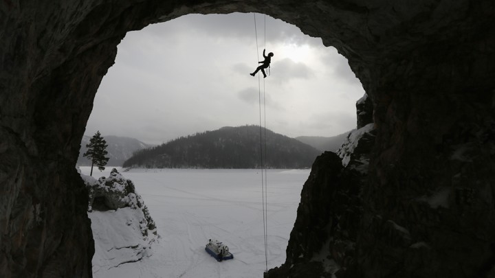 A climber belays from the top of a tall cave.