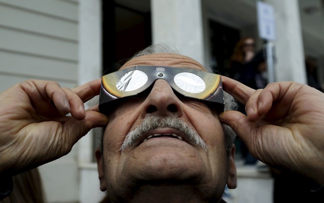 A man looks through eclipse glasses.