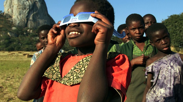 A girl looks through eclipse glasses.