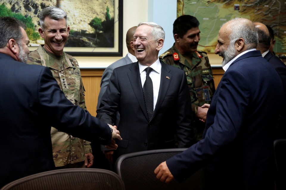 James Mattis stands in the center laughing and shaking hands with men in suits and military uniforms.
