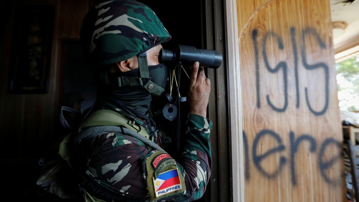 A Filipino soldier uses binoculars next to a wood panel where the words ' ISIS here' are spray-painted.