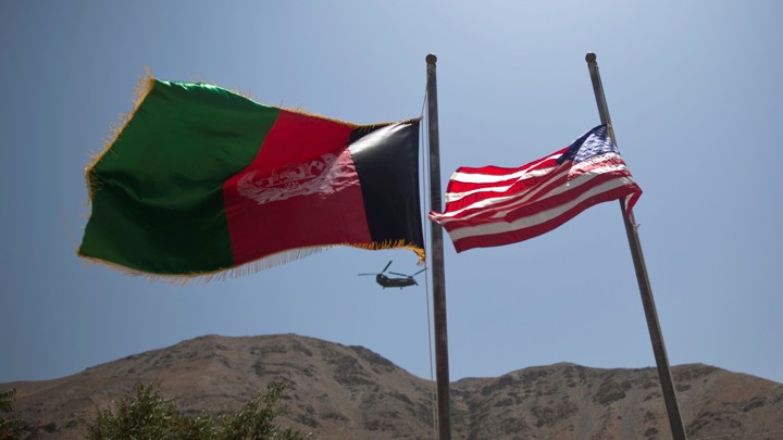 An Afghan flag flutters next to a U.S. flag with a U.S. military helicopter in the background.