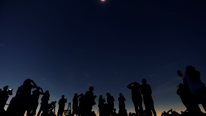 A group of people watches a solar eclipse.