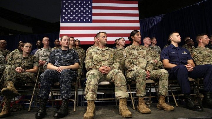 Members of the U.S. military sit in front of an American flag.