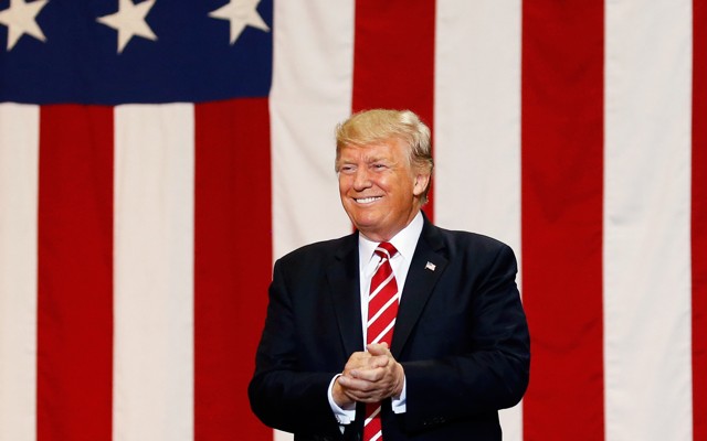 Donald Trump smiles in front of an American flag. 