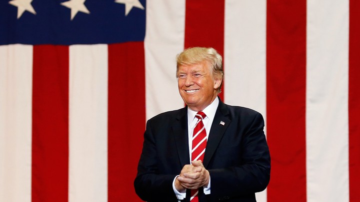 Donald Trump smiles in front of an American flag.