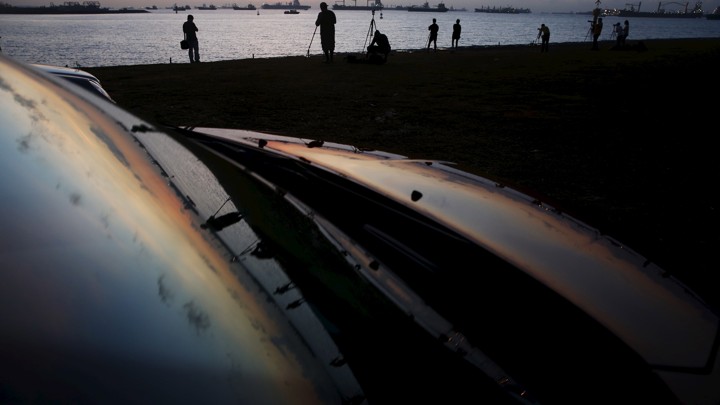 People setting up tripods reflected on a metallic surface