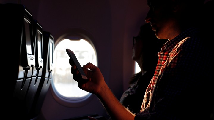 A person holds a phone while being backlit through an airplane window
