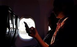 A person holds a phone while being backlit through an airplane window