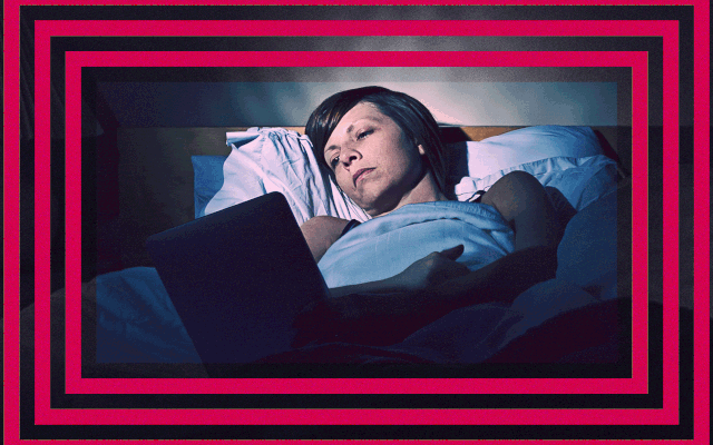 A woman lies in bed looking at a flickering screen