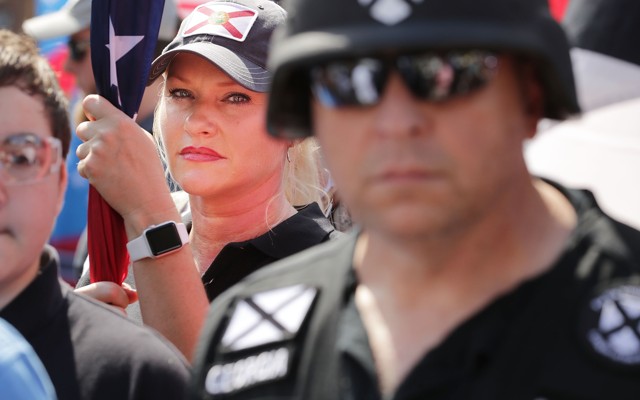Standing behind a man in a helmet, a woman holds a flag at a rally in Charlottesville, Virginia