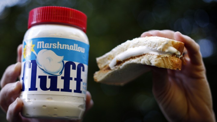 A jar of fluff next to half of a peanut butter and fluff sandwich