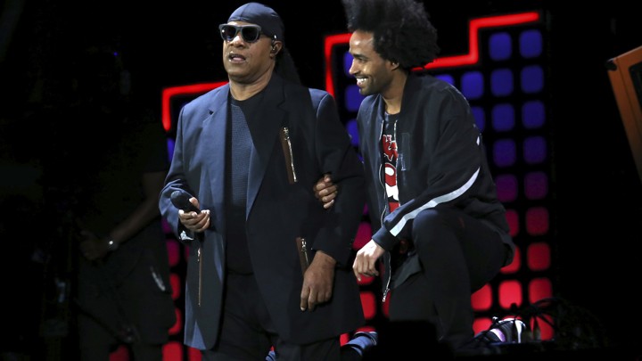 Stevie Wonder, left, kneels on stage next to his son Kwame Morris before performing at the Global Citizen Festival in Central Park on Saturday, Sept. 23, 2017, in New York.