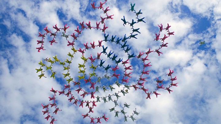 A spiraling skydiving formation against a partly cloudy sky