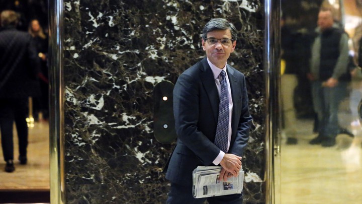 George Stephanopoulos stands in Trump tower and carries a newspaper.