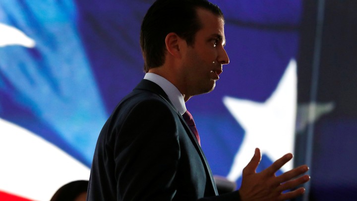 Donald Trump Jr. stands in front of an American flag.