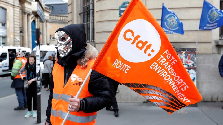 A masked demonstrator holds a flag of the French Democratic Confederation of Labour union (CFDT) in Paris during a national protest against the government's labour reforms on September 18, 2017.