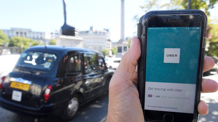 A person holds a phone with the Uber app in front of a black cab.