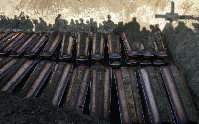 Shadows of people burying dozens of coffins in a mass grave.
