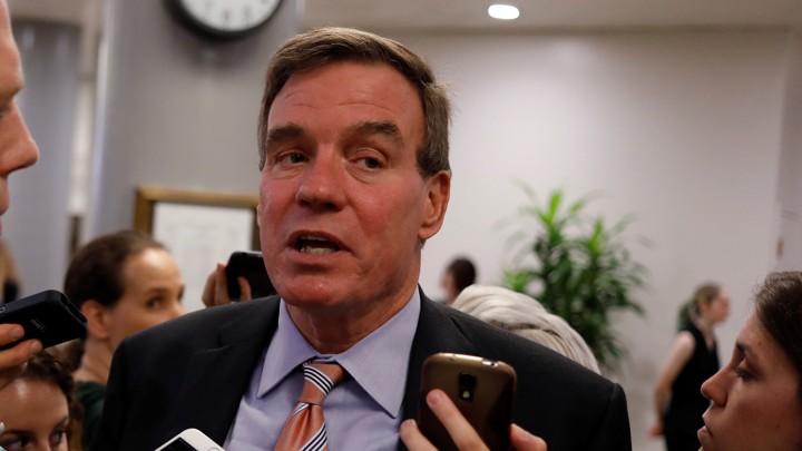 Mark Warner speaks as reporters hold up cellphones to record him.