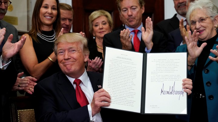 Donald Trump presents a signed executive order as an audience claps.