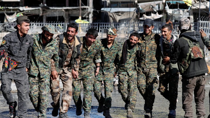 Fighters of the Syrian Democratic Forces dance along a street.