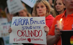 A woman at a candlelight vigil holds a sign reading "Aurora families stand with Orlando."
