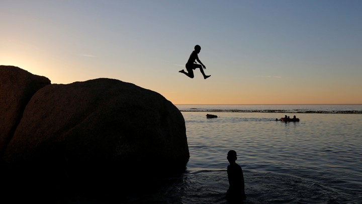 A child jumps off a rock into a body of water at sunset or sunrise